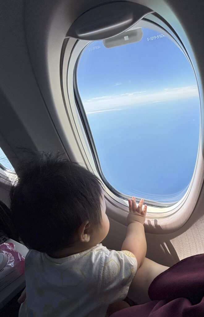 飛行機の窓の外を見つめる子どもの後ろ姿。旅の非日常感を感じさせる一枚